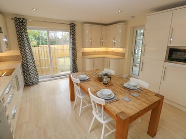 A kitchen with wooden dining table set for four near sliding glass doors with patterned curtains at Castle at The Hideaway in Tenby
