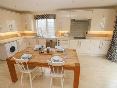 A kitchen with a wooden dining table set for four and white cabinets at Castle at The Hideaway in Tenby