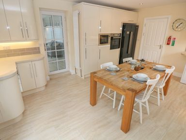 A kitchen with wooden dining table and white chairs set with dishes and glassware at Castle at The Hideaway Tenby