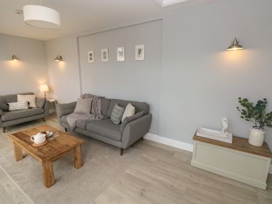 A living room with two grey sofas a wooden coffee table and a cabinet with a plant at Castle at The Hideaway in Tenby