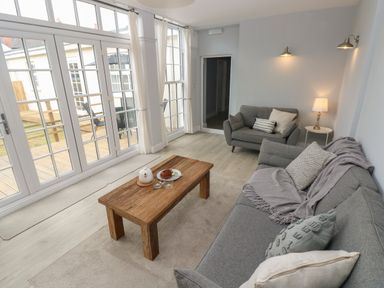 A living room with two grey sofas wooden coffee table and glass doors leading outside at Castle at The Hideaway in Tenby