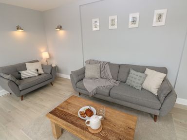 A living room with two gray sofas a wooden coffee table and framed pictures on the wall at Castle at The Hideaway in Tenby