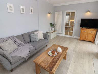 A living room with a gray sofa and wooden coffee table with a teapot and plate at Castle at The Hideaway in Tenby