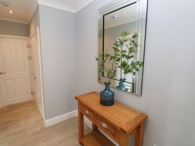 A hallway with a wooden table holding a blue vase with green branches and a large mirror on the wall at Castle at The Hideaway in Tenby