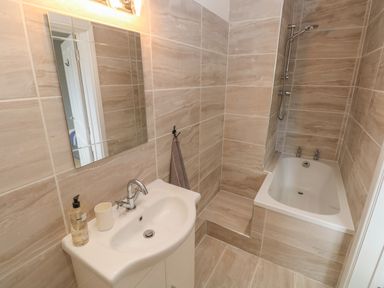 A bathroom with a sink and mirror next to a bathtub with a showerhead at Castle at The Hideaway in Tenby