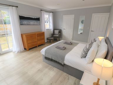 A bedroom with a bed, wooden chest of drawers, armchair, and windows at Castle at The Hideaway in Tenby