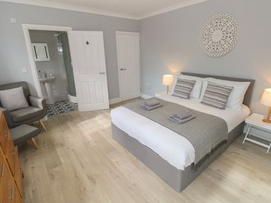A bedroom with a bed towels armchair and an open door showing a bathroom at Castle at The Hideaway in Tenby