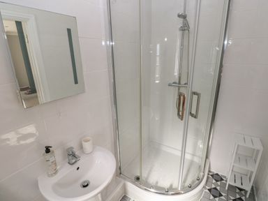 A bathroom with a sink and mirror next to a glass shower enclosure and a small shelf unit at Castle at The Hideaway in Tenby