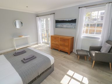 A bedroom with a bed, wooden dresser, armchair with footstool, and French doors at Castle at The Hideaway in Tenby