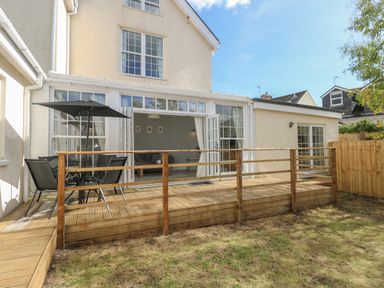 A wooden deck with a table and chairs and an umbrella outside a house with large windows and doors at Castle at The Hideaway in Tenby
