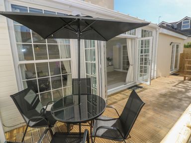 An outdoor wooden deck with a round glass table and four black chairs under a black umbrella at Castle at The Hideaway in Tenby