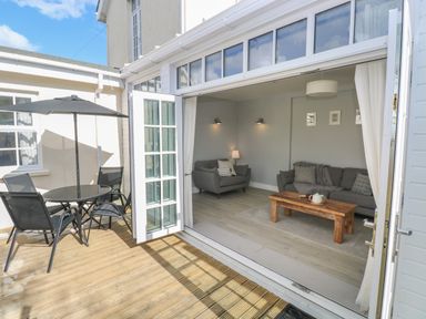 An open patio door showing a living room with sofas and a wooden coffee table and an outdoor seating area with a round table and umbrella at Castle at The Hideaway in Tenby