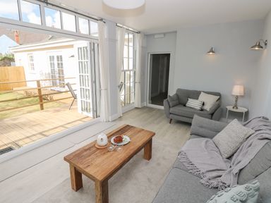 A living room with gray sofas wooden coffee table and open glass doors leading to a deck at Castle at The Hideaway in Tenby