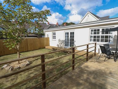 A backyard with a wooden deck and railing a tree and patio furniture at Castle at The Hideaway in Tenby