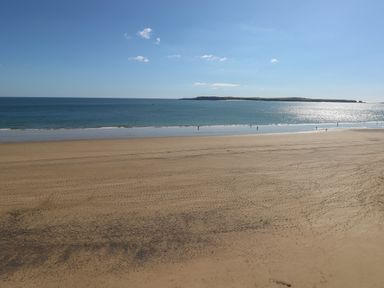 A sandy beach with footprints and waves and an island in the distance at Castle at The Hideaway in Tenby