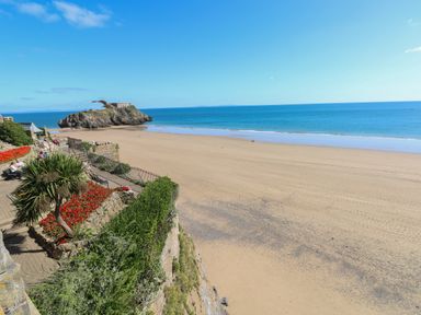 A sandy beach with a rocky island and people sitting by a garden at Castle at The Hideaway in Tenby