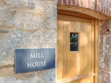 A wooden door with a small window next to a stone wall with a sign that reads mill house at Mill House Boskensoe Barns in Mawnan Smith near Falmouth