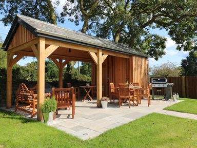 An outdoor patio with wooden furniture a covered seating area and a barbecue grill at Mill House Boskensoe Barns Mawnan Smith near Falmouth