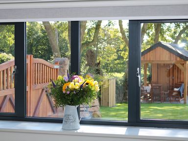 A bouquet of flowers on a windowsill overlooking a garden with a wooden gate and a wooden gazebo at Mill House Boskensoe Barns Mawnan Smith near Falmouth