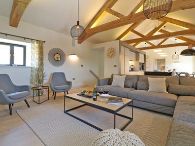 A living room with a large gray sofa two gray chairs a coffee table with wine glasses and bread beams on the ceiling at Mill House Boskensoe Barns in Mawnan Smith near Falmouth