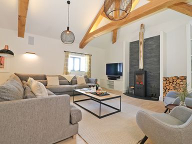 A living room with a gray sectional sofa wood burning stove and a television at Mill House Boskensoe Barns in Mawnan Smith near Falmouth