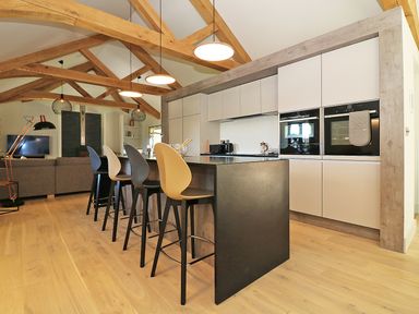 A kitchen with a black island and four bar stools under wooden beam ceilings at Mill House Boskensoe Barns Mawnan Smith near Falmouth