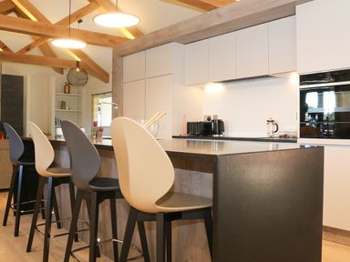 A kitchen with a black island and four bar stools with wooden beams on the ceiling at Mill House Boskensoe Barns in Mawnan Smith near Falmouth