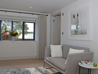 A sitting room with a sofa white cushions a window with curtains a side table with a book glasses and an apple and a picture of a horse at Mill House Boskensoe Barns in Mawnan Smith near Falmouth