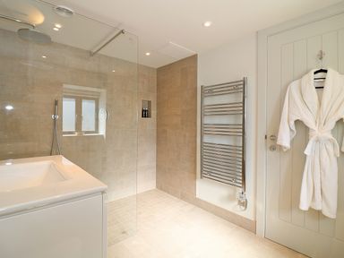 A bathroom with a walk in shower tub towel radiator and a bathrobe hanging on a door at Mill House Boskensoe Barns in Mawnan Smith near Falmouth