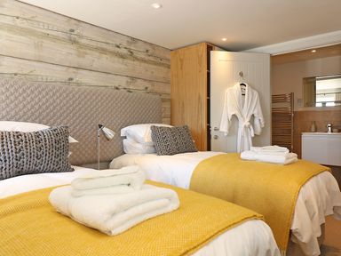 A bedroom with two beds yellow blankets and white towels a bathrobe hanging on the door at Mill House Boskensoe Barns in Mawnan Smith near Falmouth