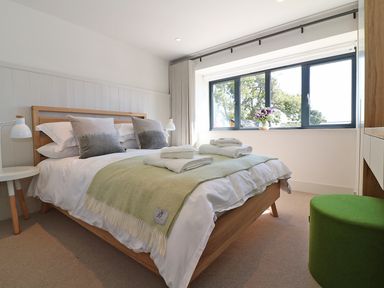 A bedroom with a wooden bed frame white bedding green blanket and folded towels near a window with flowers at Mill House Boskensoe Barns in Mawnan Smith near Falmouth