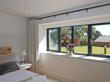A bedroom with a bed a bedside table and a window overlooking a garden at Mill House Boskensoe Barns in Mawnan Smith near Falmouth