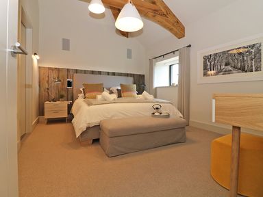 A bedroom with a bed, bedside tables, a bench, a window, and a framed picture at Mill House Boskensoe Barns Mawnan Smith near Falmouth