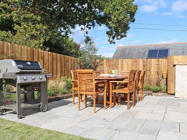An outdoor patio with a wooden dining table and chairs and a barbecue grill at Mill House Boskensoe Barns in Mawnan Smith near Falmouth