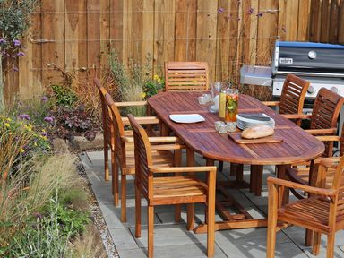 A wooden outdoor dining table with six chairs next to a barbecue grill and garden at Mill House Boskensoe Barns Mawnan Smith near Falmouth