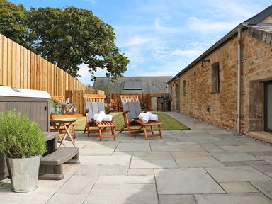 An outdoor patio with reclining wooden chairs and rolled towels next to a stone building and wooden fence at Mill House Boskensoe Barns Mawnan Smith near Falmouth