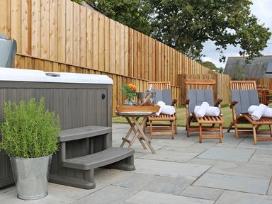 An outdoor patio with a hot tub a potted plant a small table with drinks and wooden lounge chairs with towels at Mill House Boskensoe Barns Mawnan Smith near Falmouth