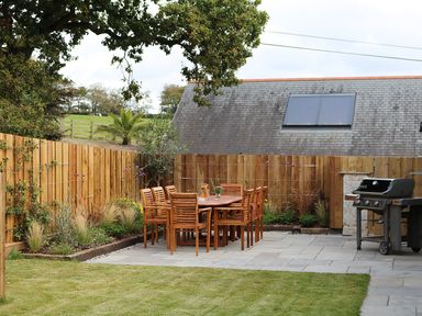 A backyard with a wooden dining table and chairs a barbecue and a wooden fence at Mill House Boskensoe Barns in Mawnan Smith near Falmouth