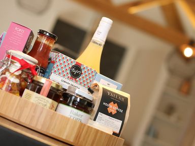 A wooden tray with jars of jam and coffee a bottle of juice and other food items