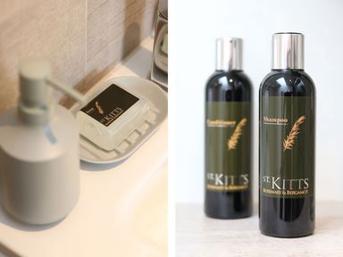 A soap bar in a soap dish beside a lotion dispenser and two bottles of shampoo and conditioner labeled St Kitts Rosemary and Bergamot