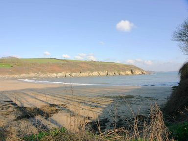 A sandy beach with sea and cliffs under a blue sky at Mill House Boskensoe Barns in Mawnan Smith near Falmouth