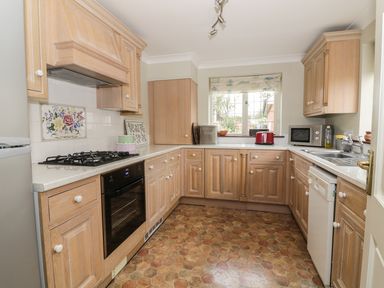 A kitchen with wooden cabinets a gas stove an oven a microwave a dishwasher and a window at The Lodge off High Street in Hadleigh