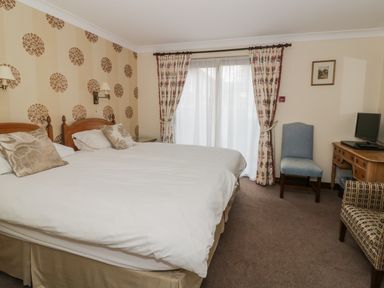 A bedroom with two beds a wooden desk a chair and patterned curtains at The Lodge off High Street in Hadleigh