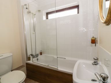 A bathroom with a bathtub shower combination a toilet and a sink with a mirror at The Lodge off High Street in Hadleigh