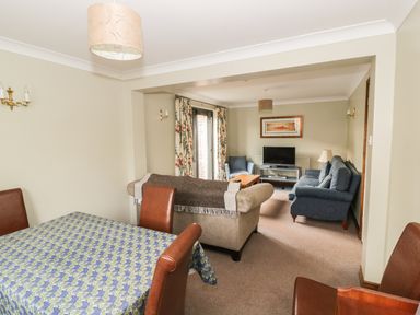 A dining table with chairs and a living room with sofas and a television at The Lodge off High Street Hadleigh