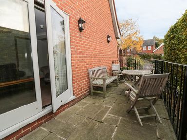 An outdoor patio with wooden chairs a round table stone flooring and black railing at The Lodge off High Street in Hadleigh