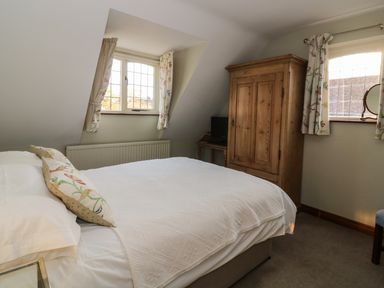 A bedroom with a double bed a wooden wardrobe a small table with a TV and two windows with floral curtains at The Lodge off High Street in Hadleigh