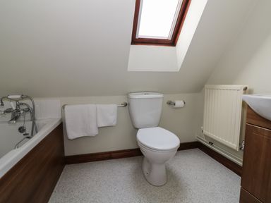 A bathroom with a toilet, bathtub, sink, towel rail, radiator, and skylight at The Lodge off High Street in Hadleigh