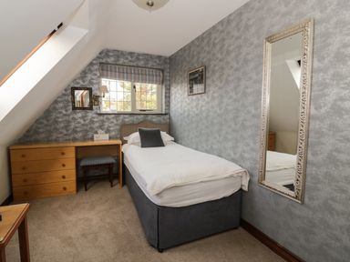 A bedroom with a single bed a wooden desk a chair and a mirror on the wall at The Lodge off High Street in Hadleigh