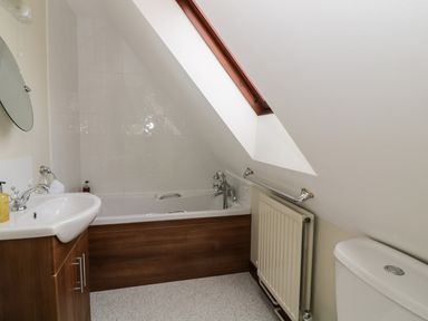 A bathroom with a bathtub under a sloped ceiling skylight a sink with wooden cabinet a radiator and a toilet at The Lodge off High Street in Hadleigh